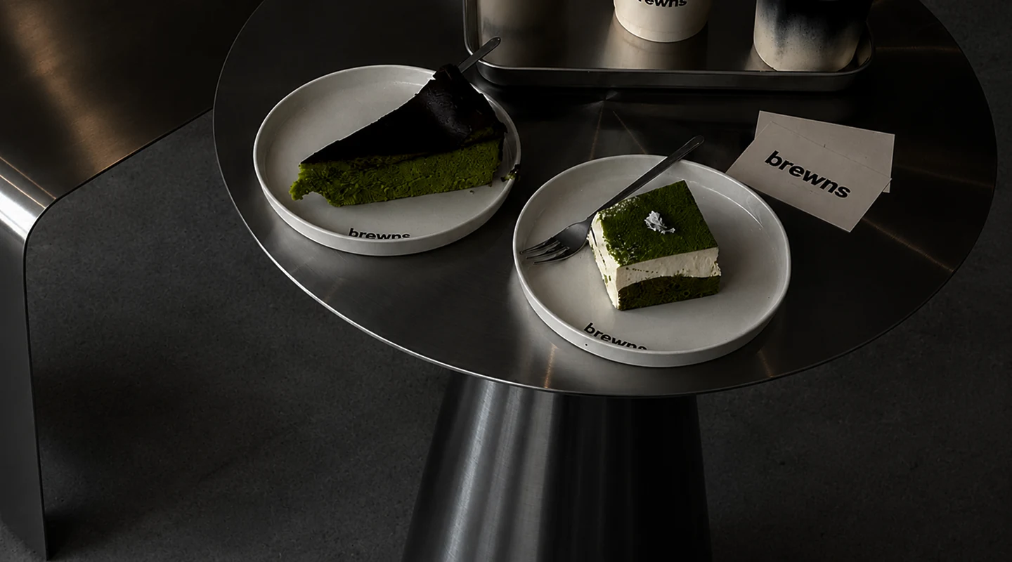 Two matcha cakes on brewns plates on a steel side table